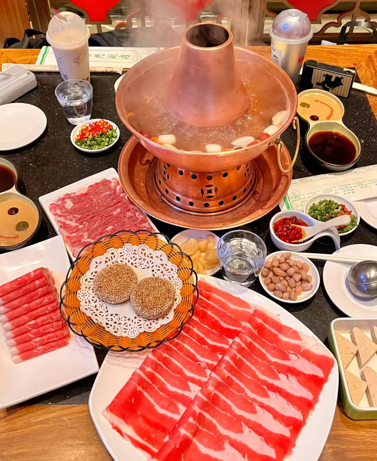Traditional Beijing hot pot with sliced lamb, vegetables, and dipping sauces on the table.jpg